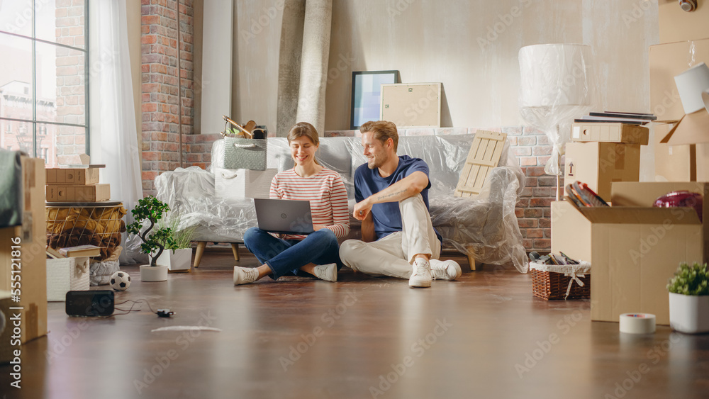 Happy Young Homeowners: Lovely Couple Sitting on Floor of the Newly Purchased Apartment Use Laptop C