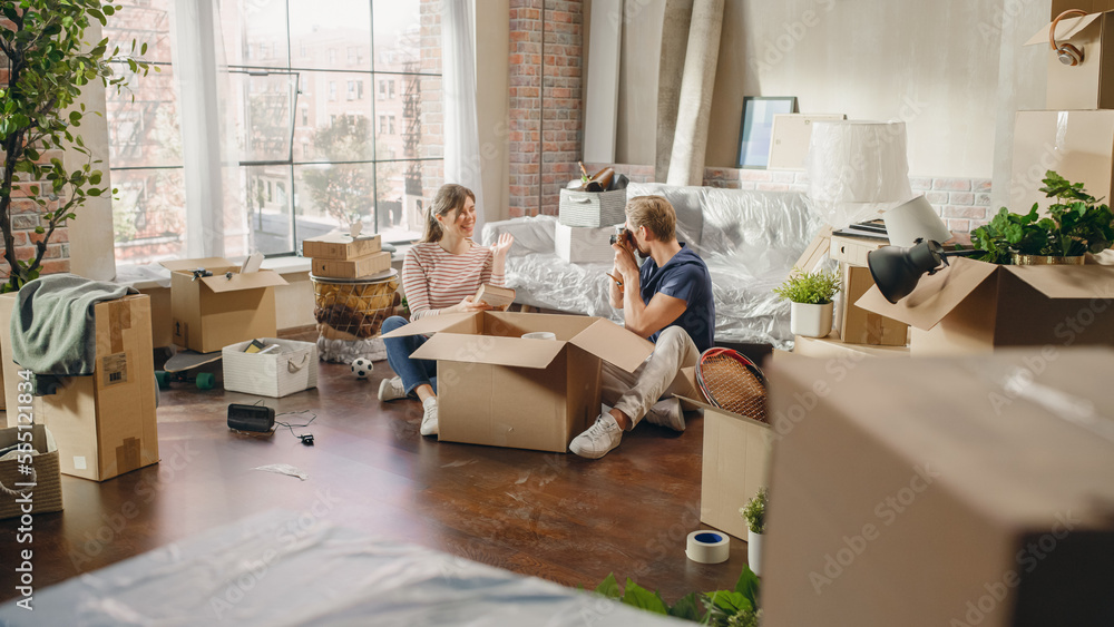 Happy Homeowners Moving In: Lovely Couple Sitting on the Floor of the Cozy Apartment Unpacking Cardb