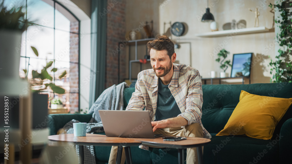 Portrait of Smiling Middle Aged Man Working from Home on a Laptop Computer in Sunny Cozy Apartment. 