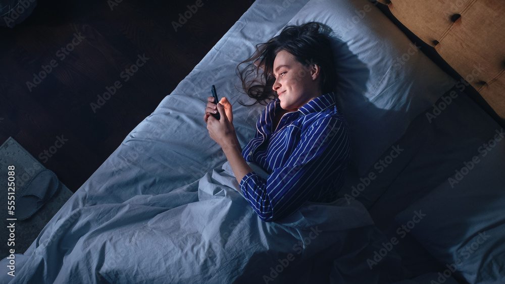 Top View Bedroom Apartment: Beautiful Young Woman Using Smartphone in Bed at Night. Smiling Girl Bro