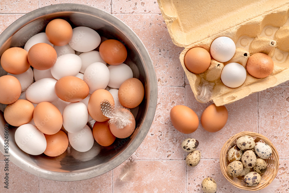 Eggs in metallic bowl on beige background. Top view of raw brown eggs and white eggs in open egg box