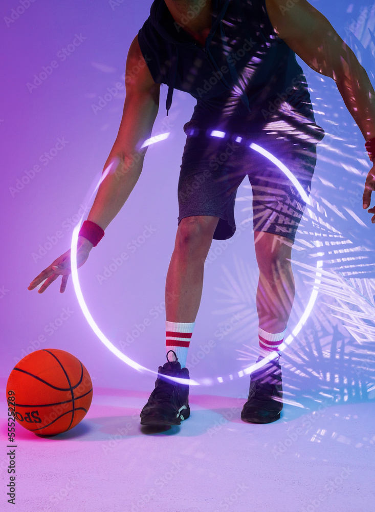 Low section of biracial basketball player dribbling ball by illuminated circle and plants