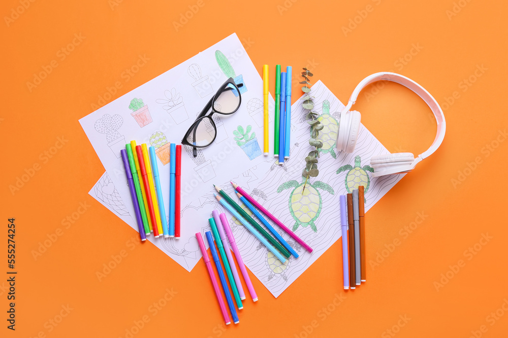 Coloring pages, felt-tip pens, pencils, headphones and eucalyptus on orange background