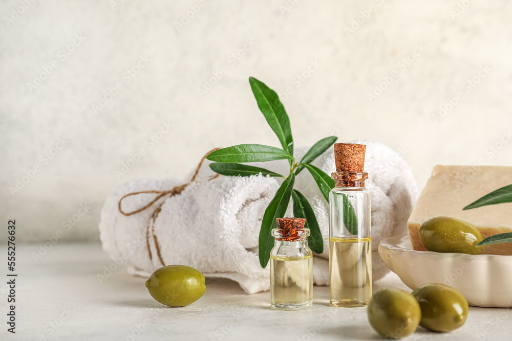 Bottles of oil, green olives, soap bar and towels on light background