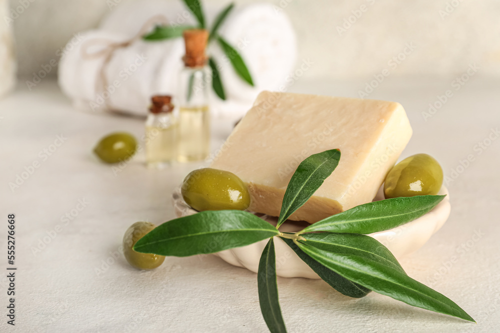 Soap bar with green olives and plant branch on light background, closeup