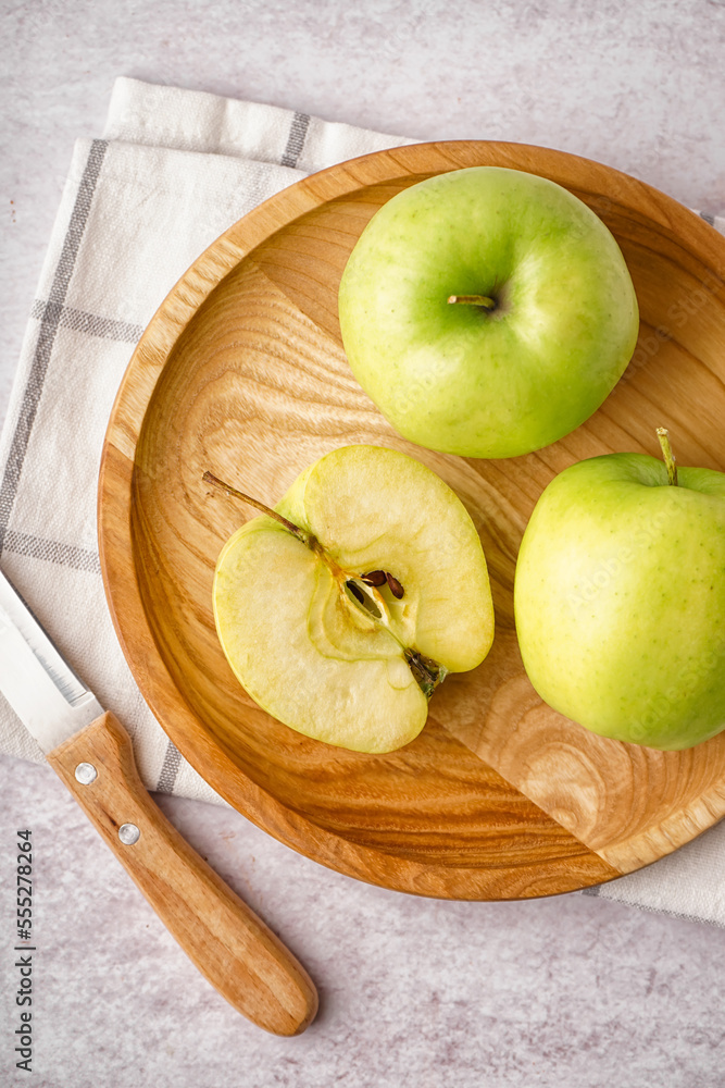 Wooden plate with fresh green apples on light background, closeup