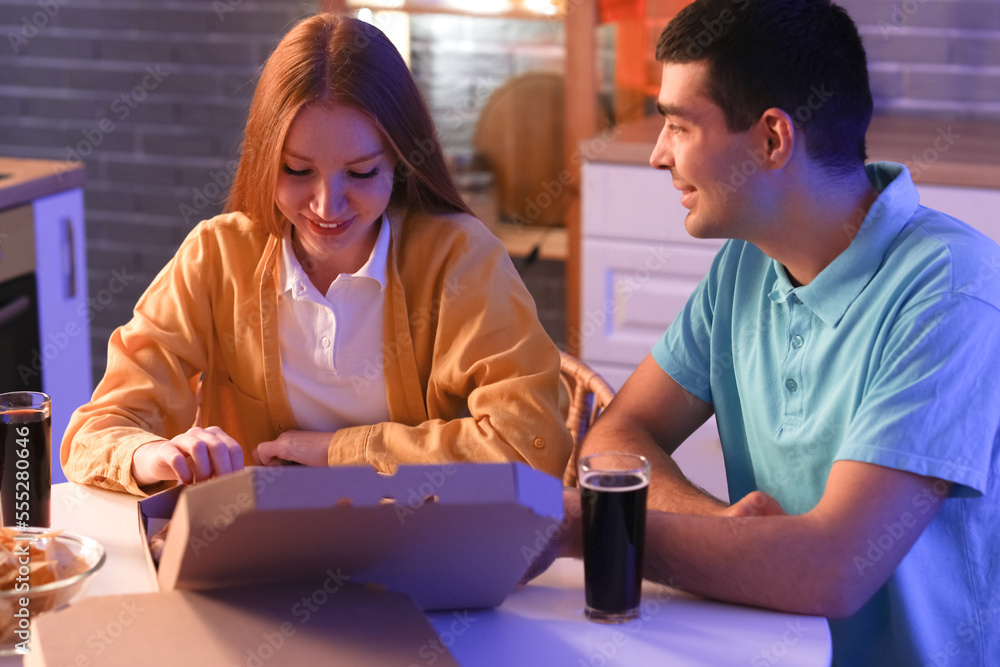 Young couple eating tasty pizza in kitchen at night