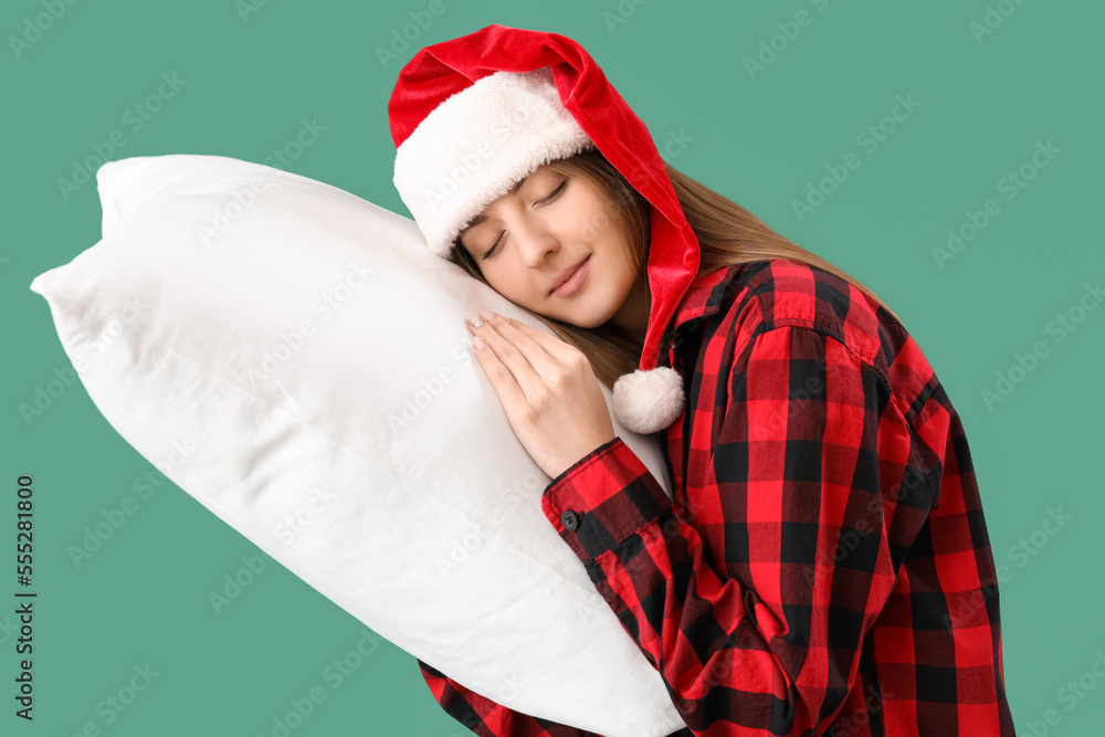 Sleepy young woman in Santa hat with pillow on green background