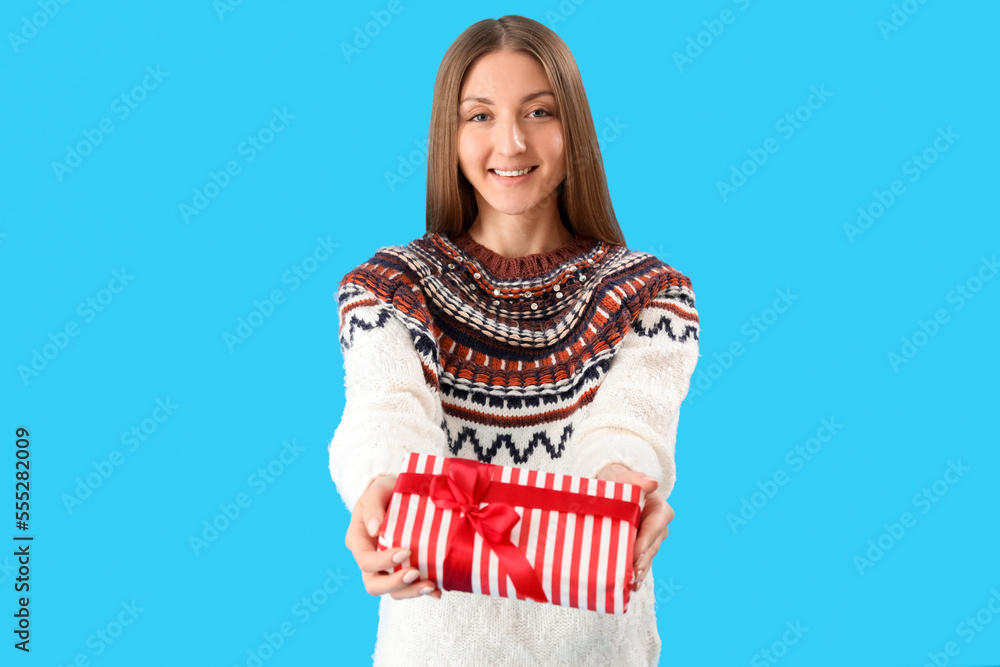 Young woman in sweater with Christmas gift on blue background