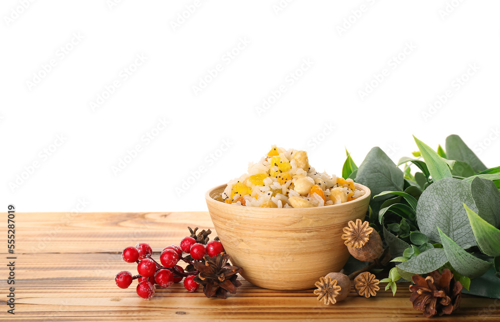 Bowl of rice Kutya, berries, flowers and Christmas wreath on table against white background