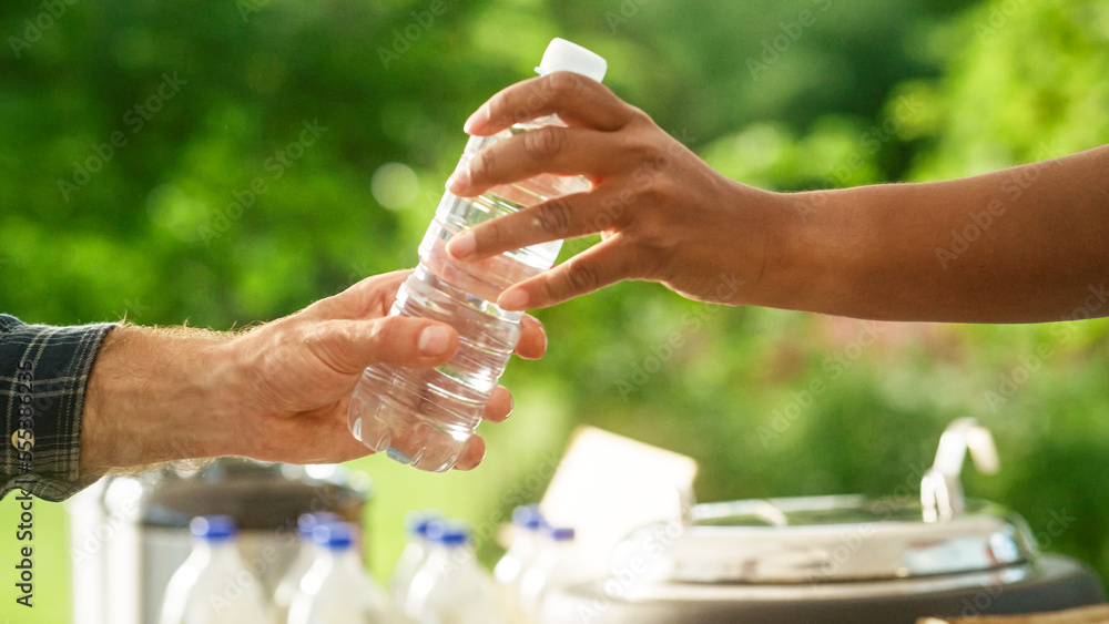 Close Up of a Anonymous Person Handing Over a Water Bottle to Another Person. Green Background in Na