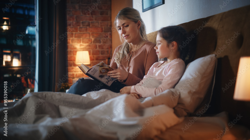 Mother Reading a Fairytale to Her Lovely Small Daughter in Bed Before Going to Sleep. Young Beautifu