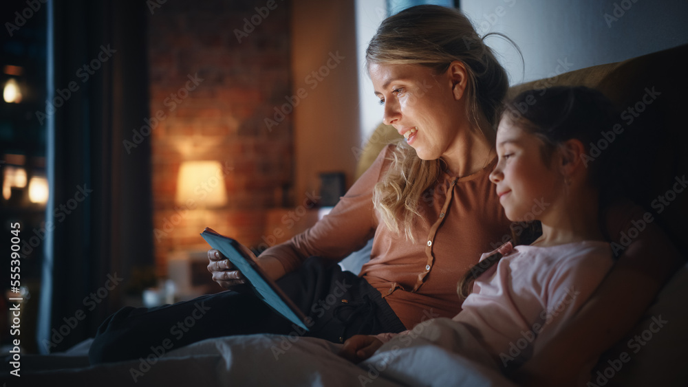 Mother Reading a Fairytale from a Tablet Computer to Her Lovely Daughter in Bed Before Going to Slee