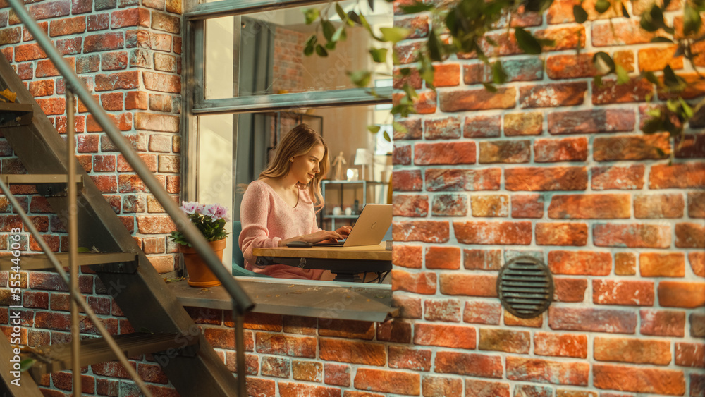 Portrait of a Young Woman Working on Laptop Computer while Sitting at Home in a Multi-Storey Brick H