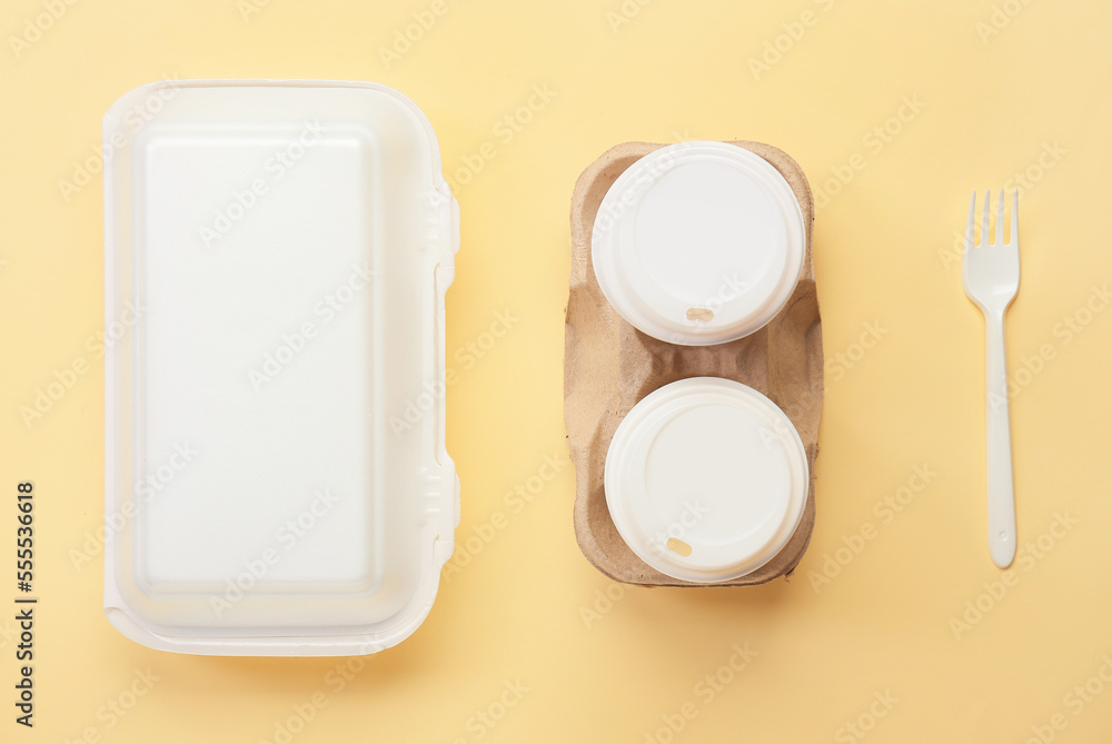 Food box, paper cups and fork on color background