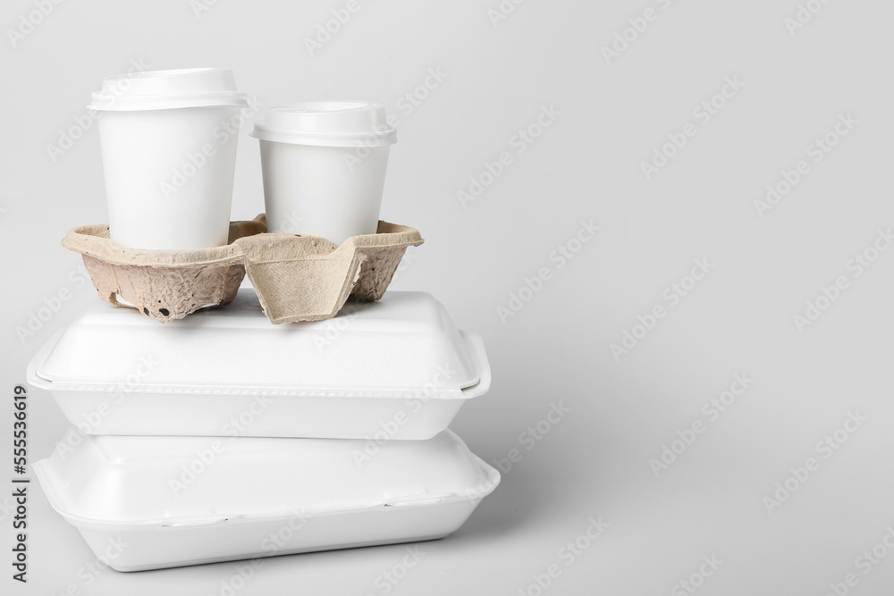 Stack of food boxes and holder with paper cups on light background