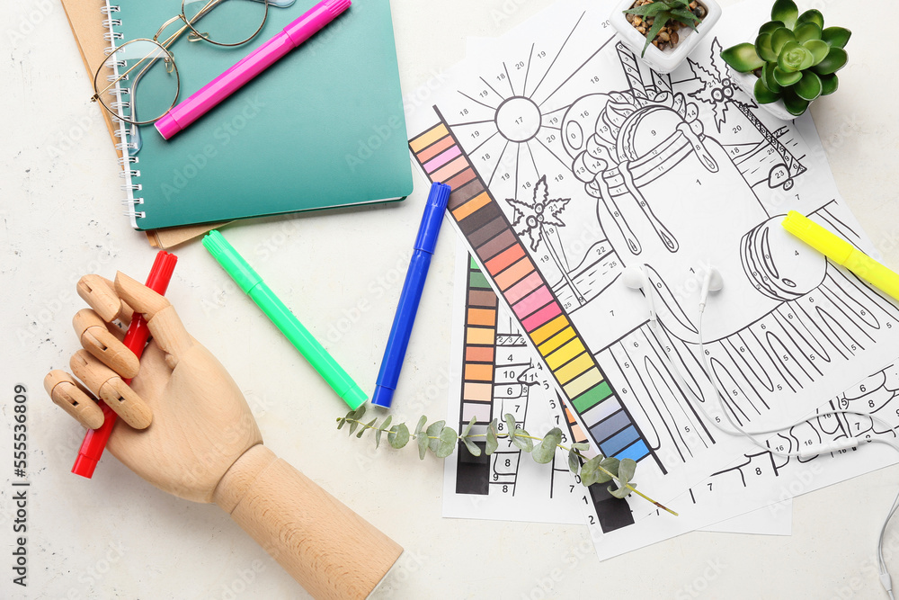 Coloring pages, felt-tip pens, wooden hand, notebooks and eyeglasses on white background