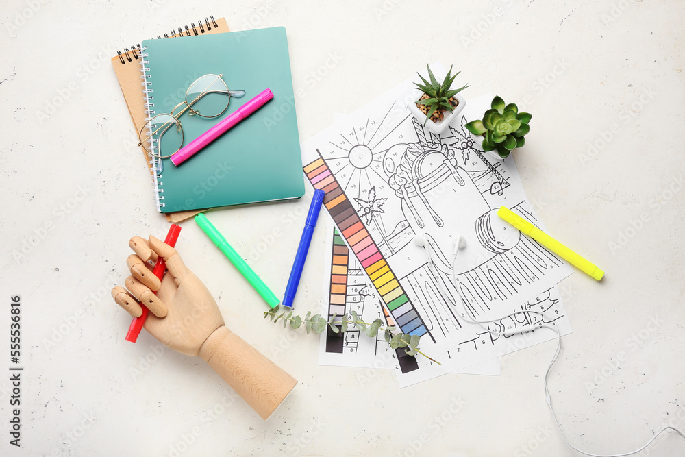 Coloring pages, felt-tip pens, wooden hand, notebooks and eyeglasses on white background