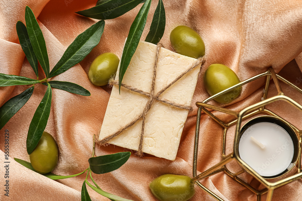 Soap bar with green olives and plant branches on color fabric background