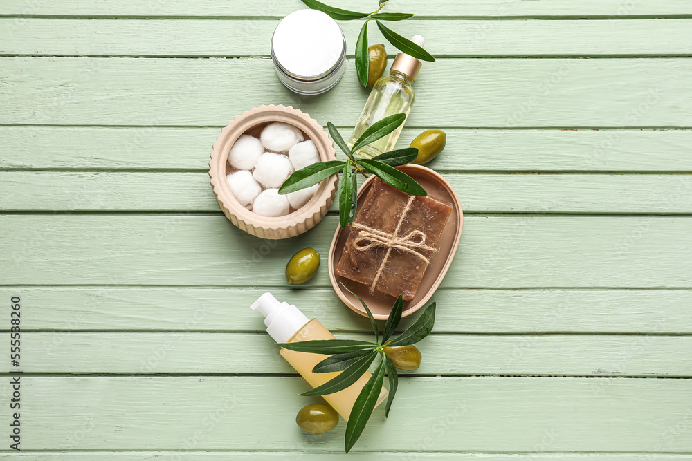 Natural cosmetics with olives, cotton balls and plant branches on green wooden background