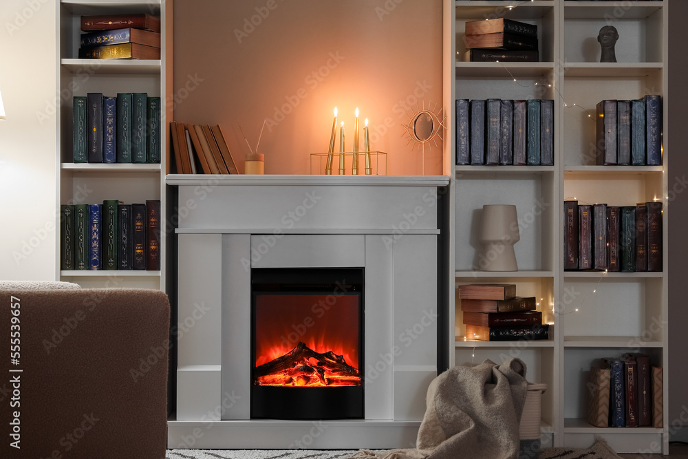 Interior of living room with fireplace, burning candles and bookshelves