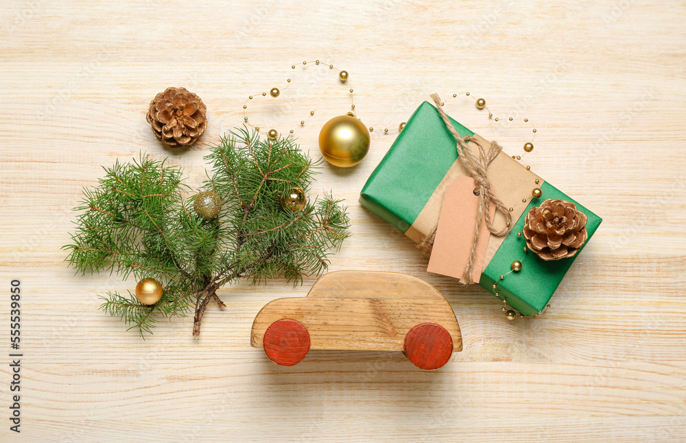 Composition with toy car, coniferous branches, gift box and decorations on wooden background