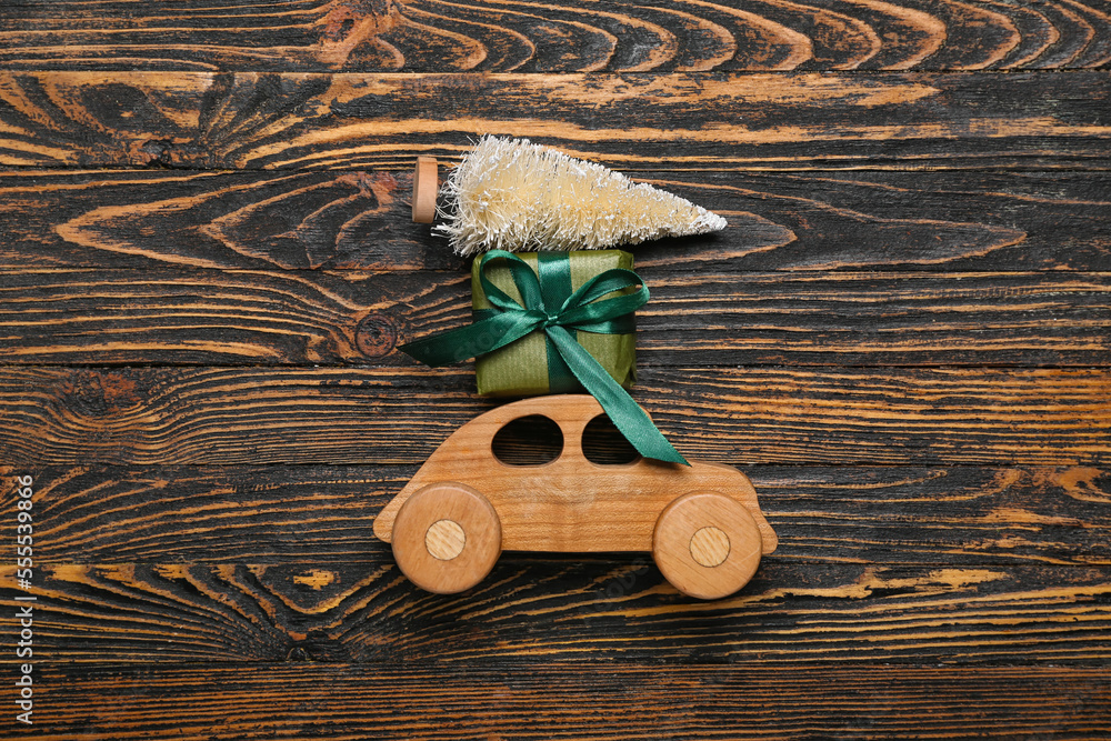 Toy car with Christmas gift and tree on wooden background