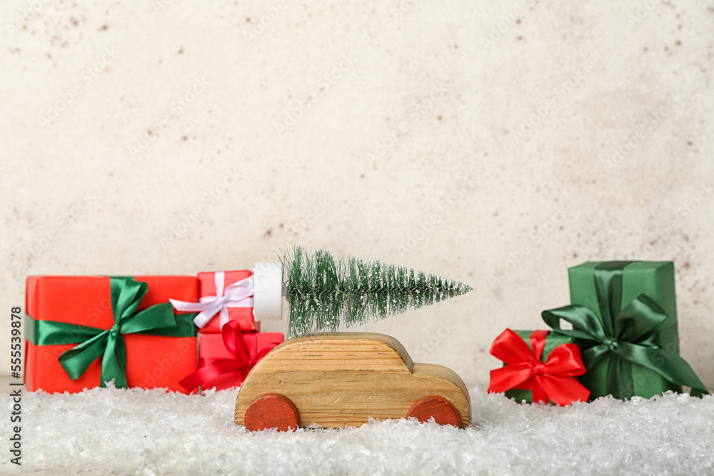 Wooden toy car with Christmas tree and gifts in snow against light background