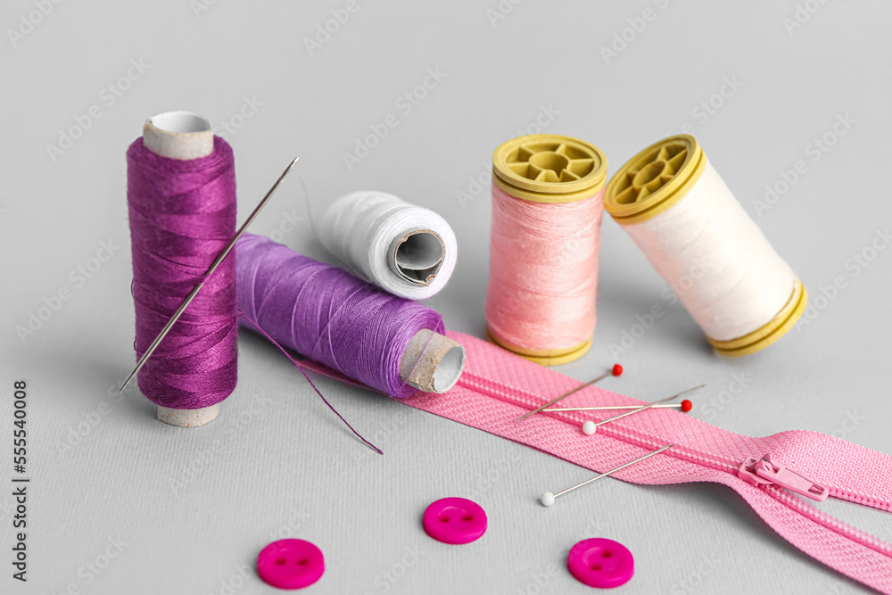 Set of sewing supplies with thread spools on grey background