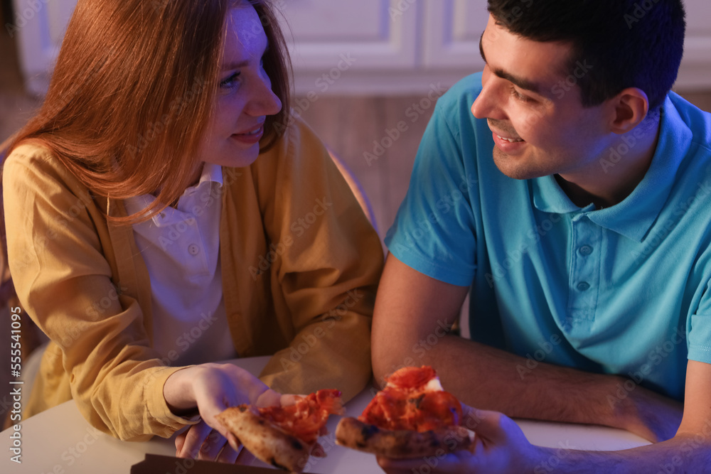 Young couple eating tasty pizza in kitchen at night, closeup