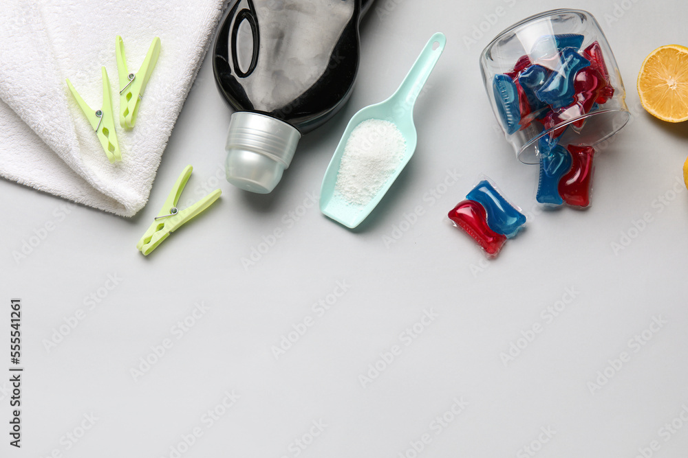 Laundry detergents, scoop and clothespins on grey background