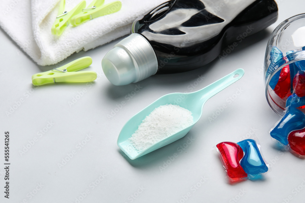 Laundry detergents, scoop and clothespins on grey background