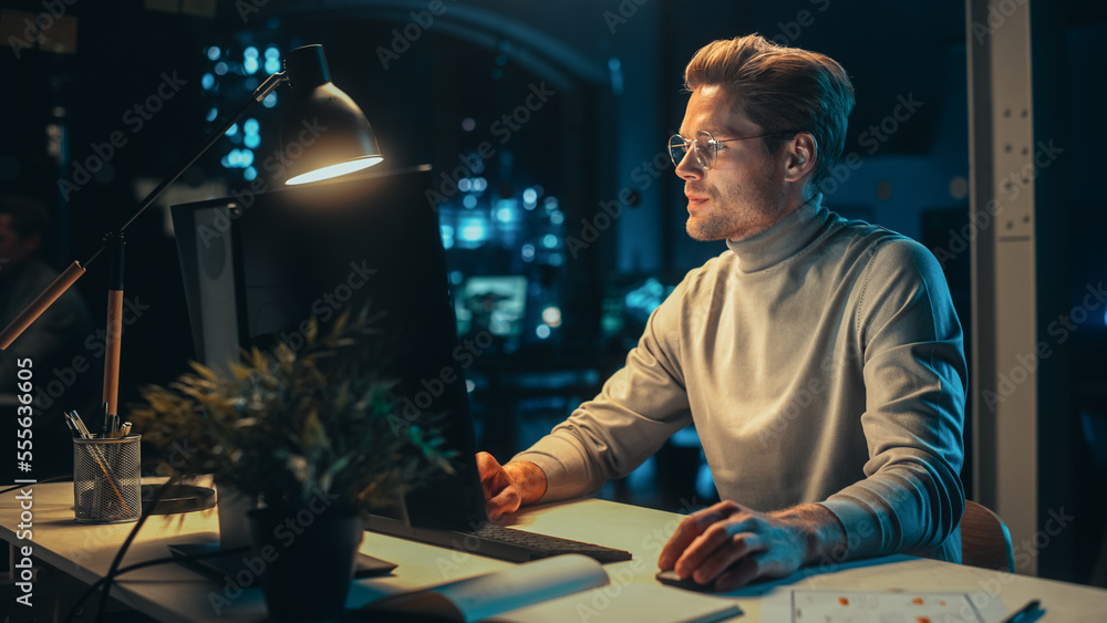 Handsome Man Working on Desktop Computer in a Company Office at Night. Young Specialist Analyzing Re