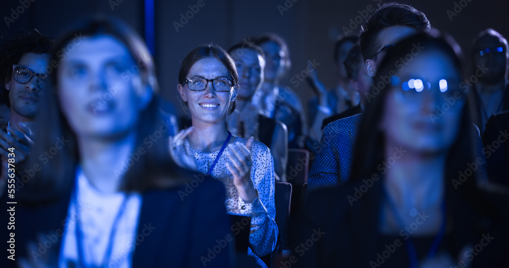 Attractive Female Sitting in a Dark Crowded Auditorium at a Tech Conference. Young Woman Applauding 