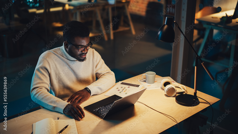 Handsome Manager Sitting at a Desk in Creative Office. Young Stylish Black Man in White Jacket Using