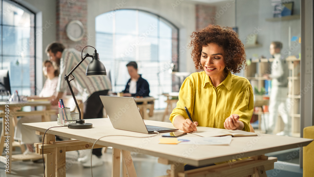 Portrait of Young Biracial Woman Taking Notes at Her Desk While Looking for References on the Laptop