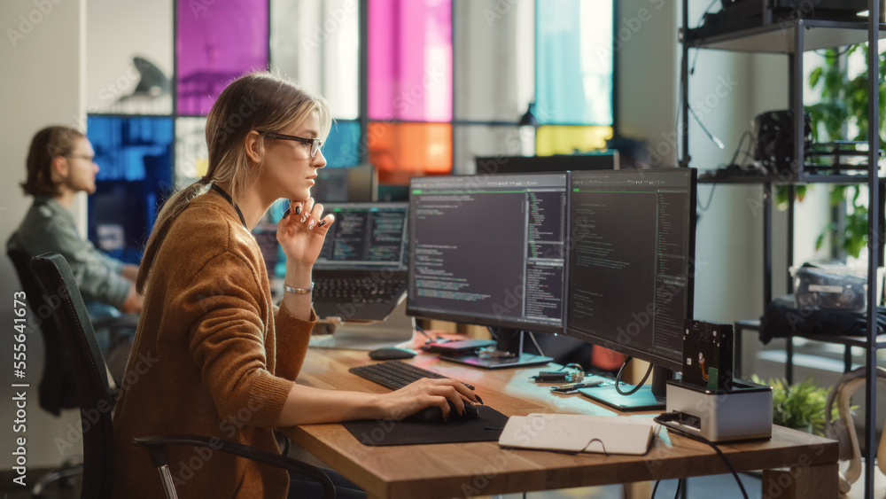 Caucasian Woman Writes Lines of Code on Desktop PC with Multiple Displays and a Laptop in Stylish Of