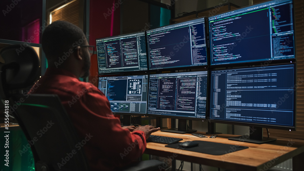 黑人网络安全专家在黑暗办公室用六台显示器在台式电脑上编码。非洲