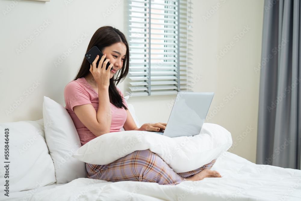 Asian businesswoman talk on phone and typing laptop keyboard in house. 