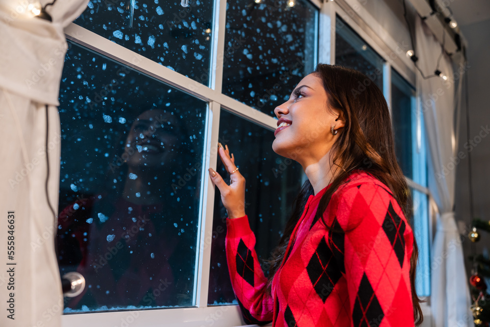 Caucasian woman look through the window and admiring first snow flakes. 