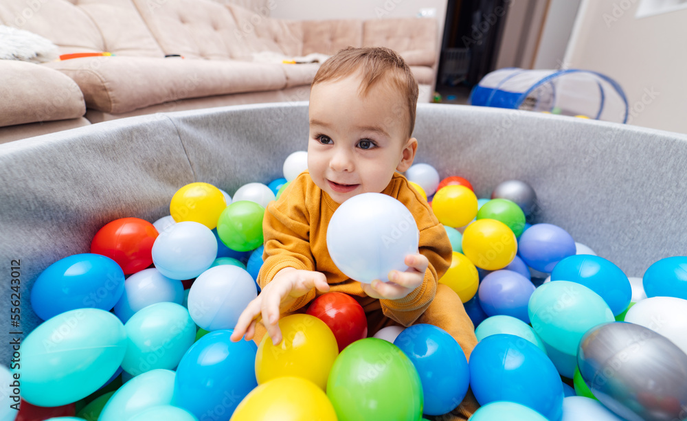 Happy child playing at colorful plastic balls. Cute baby boy having fun in ball pit. Activity toys f