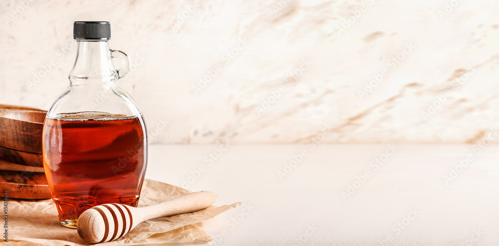 Bottle of tasty maple syrup and honey dipper on light background with space for text