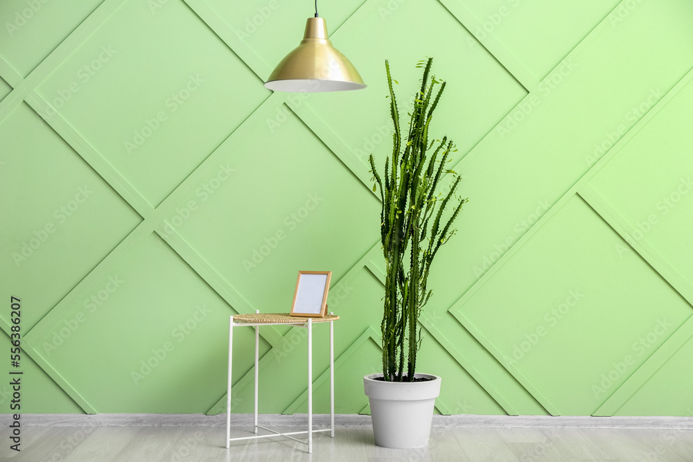 Table with blank photo frame and cactus near green wall in room