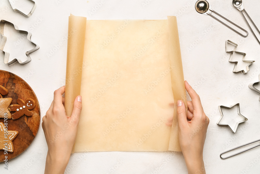 Female hands with baking paper and different cookie cutters on light background