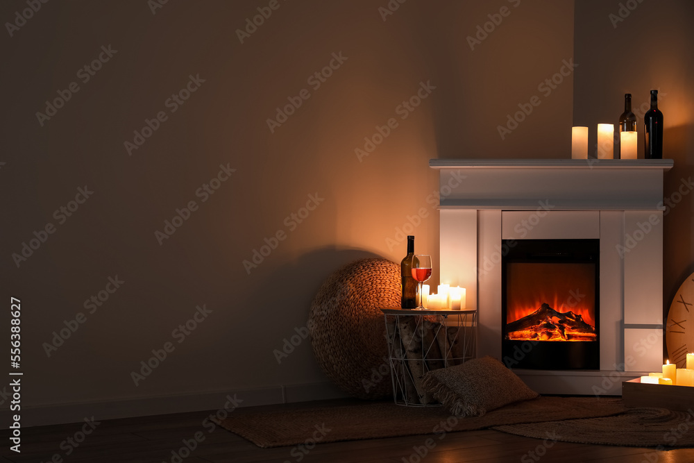 Interior of dark living room with fireplace, burning candles and wine