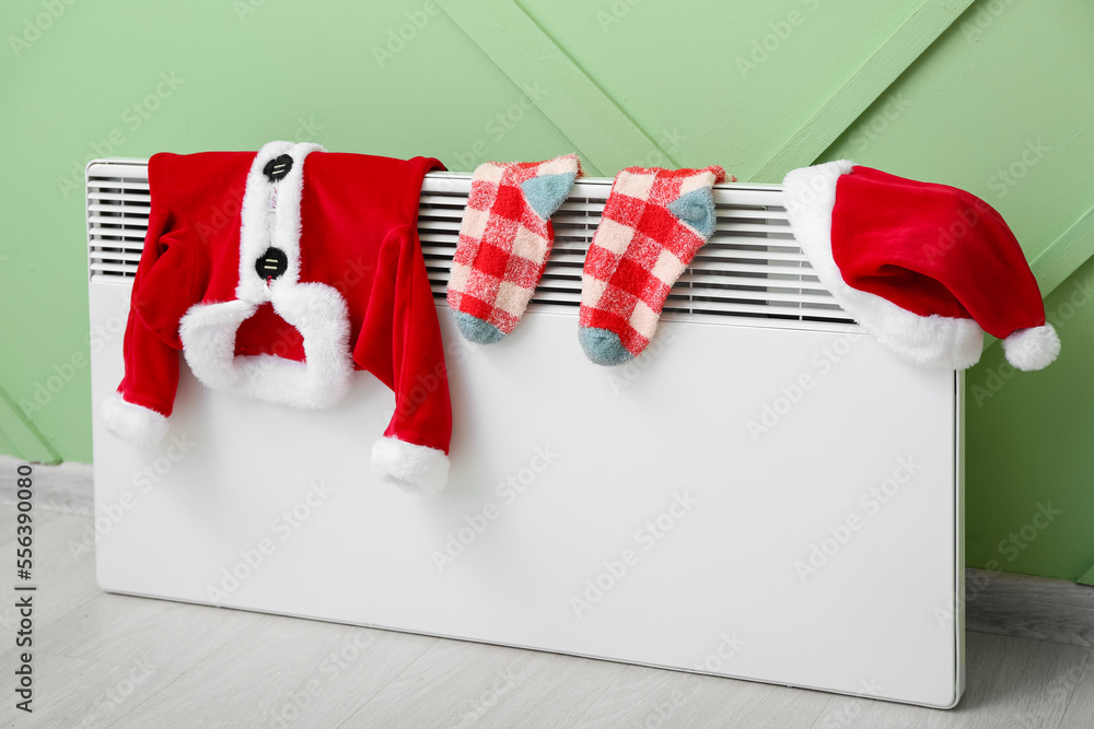 Baby Santa costume, socks and hat drying on electric radiator near green wall