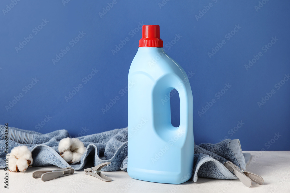 Laundry detergent and towel with beautiful flowers on table against blue background