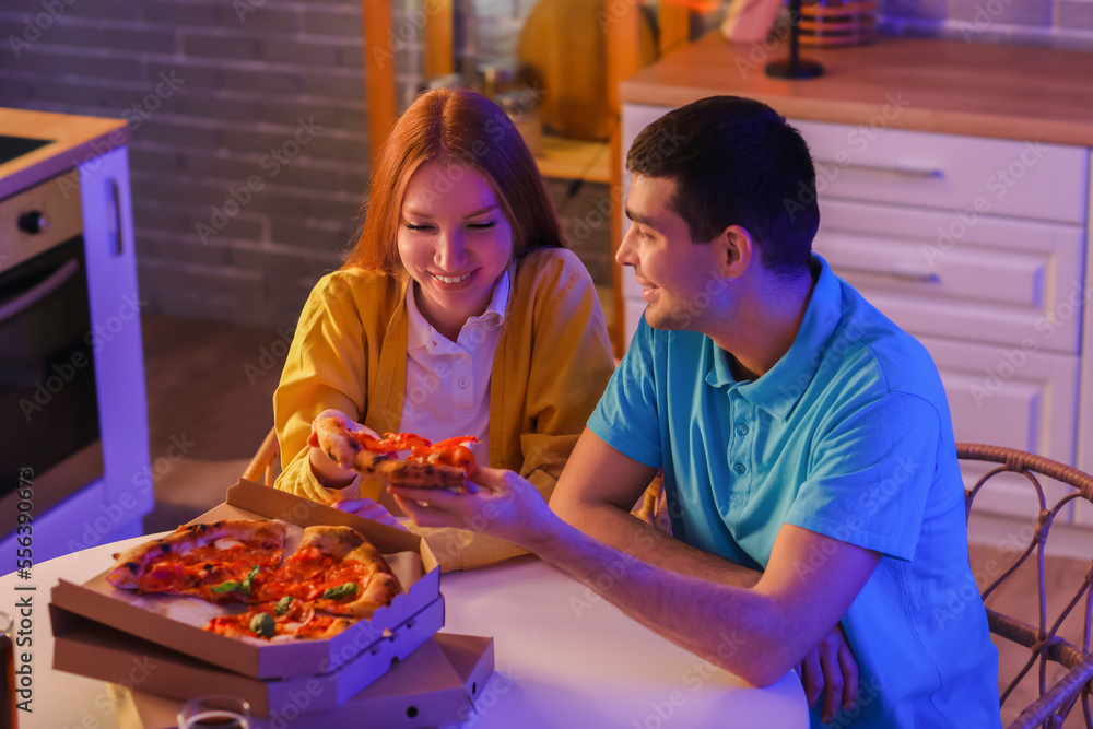 Young couple eating tasty pizza in kitchen at night