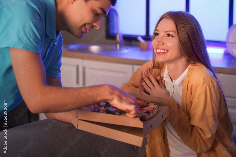 Young man brought pizza to his girlfriend in kitchen at night