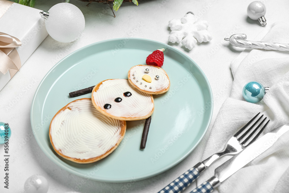 Plate with tasty snowman pancakes and Christmas decorations on light background